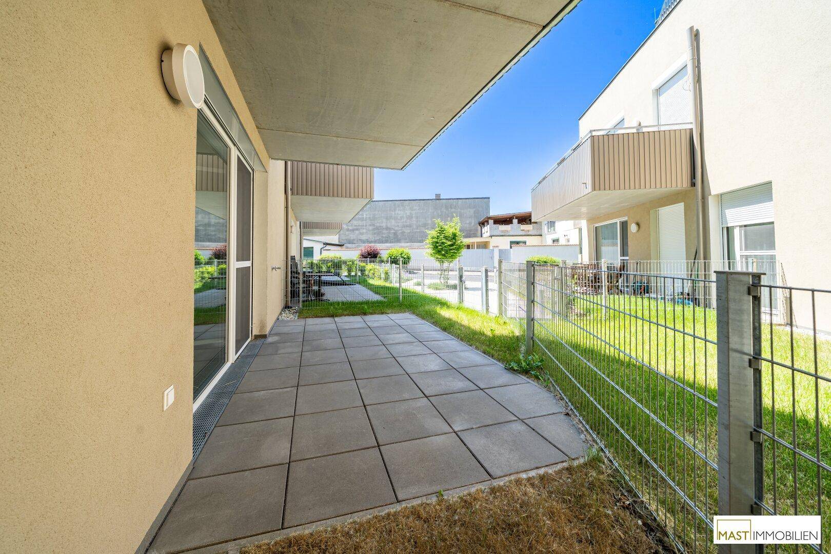 Eine geräumige Terrasse mit angrenzendem Gartenbereich, umgeben von weiteren Gebäuden der Wohnanlage.