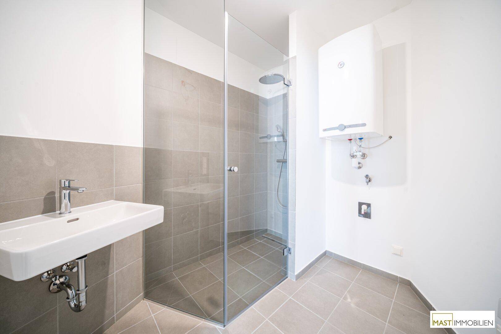 Modernes Badezimmer mit begehbarer Dusche, Einzelwaschbecken und grauen Fliesen.