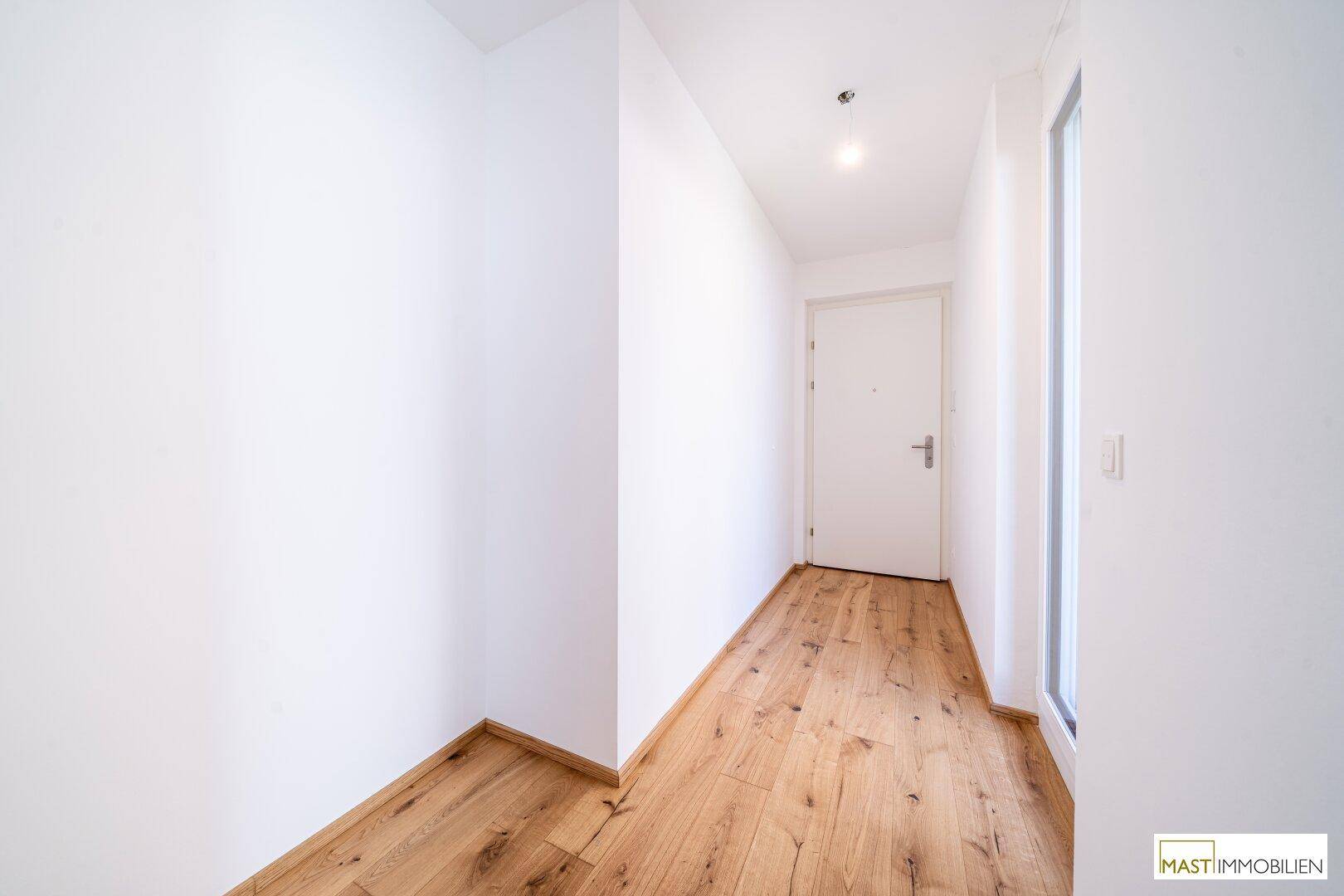 Heller Flur mit Holzboden und weiß gestrichenen Wänden, führt zum Eingangsbereich.