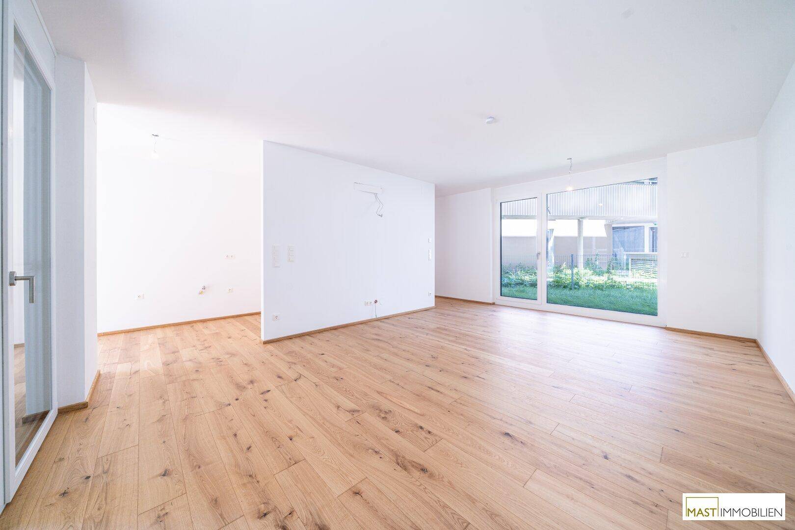 Geräumiges, leeres Wohnzimmer mit großen Fenstern und Blick auf den Gartenbereich.