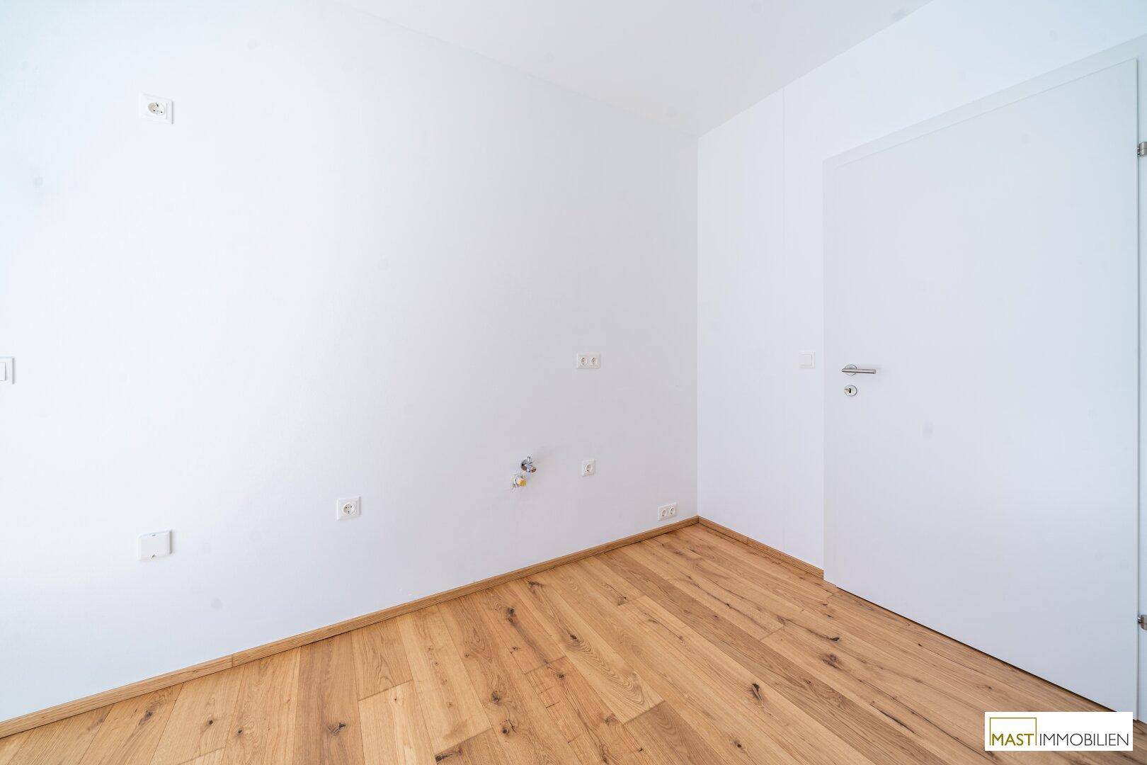 Leerer Raum mit Holzboden und Anschlüssen, bereit für die Installation einer Küche oder Waschküche.
