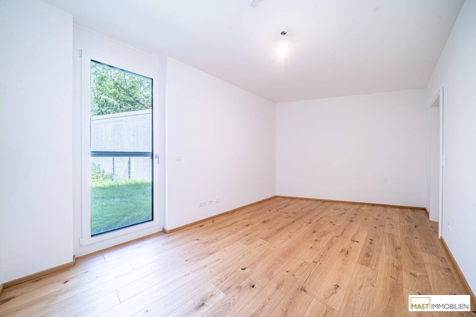 Helles Schlafzimmer mit Holzboden und Zugang zu einem kleinen Gartenbereich.