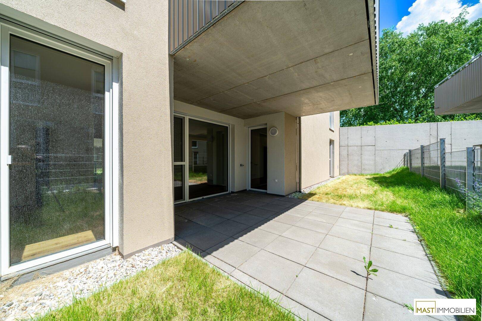 Sonniger Terrassenbereich mit Steinplatten und angrenzendem Rasen, ideal zum Entspannen.