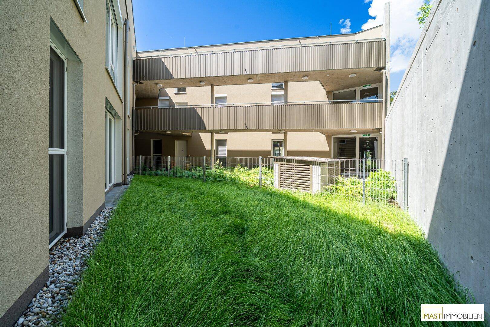 Gepflegter Gartenbereich zwischen modernen Gebäuden mit üppigem Grün und Balkonen.