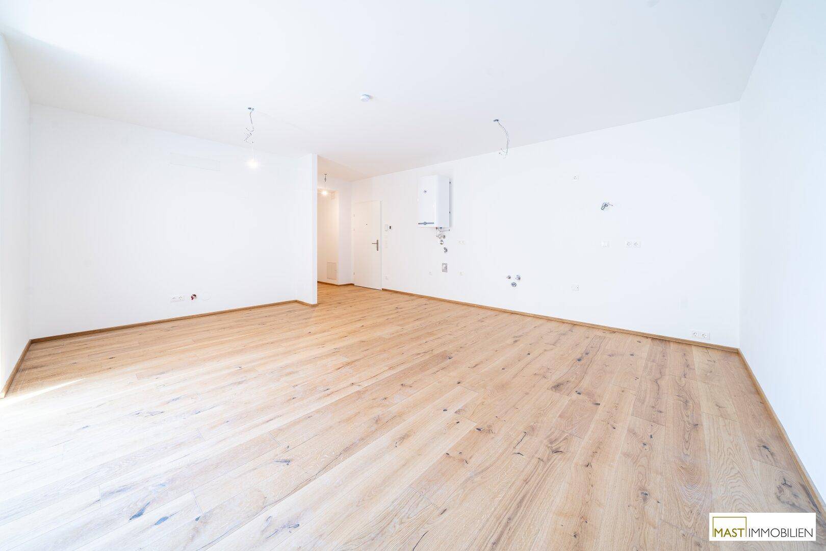 Geräumiger, unmöblierter Wohnbereich mit hellem Holzboden und weißen Wänden in einem Neubau.