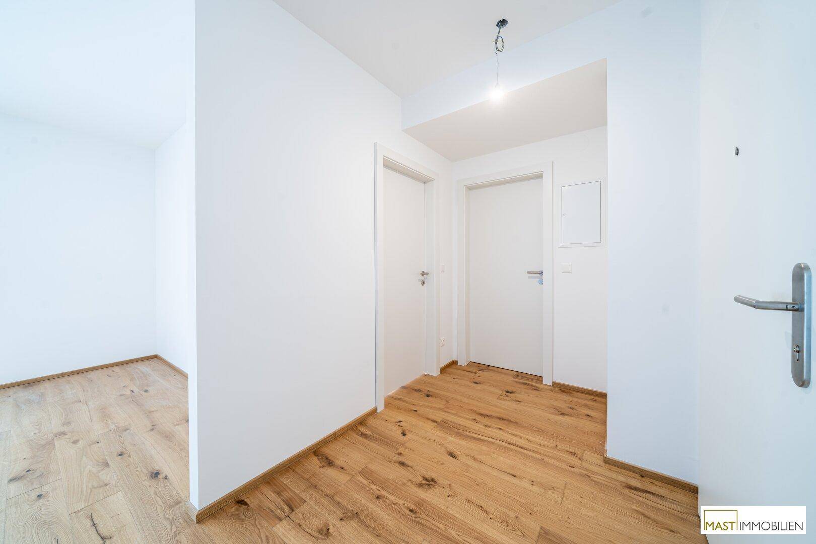 Heller Eingangsbereich mit Holzboden und weißen Türen, der zu weiteren Räumen führt.