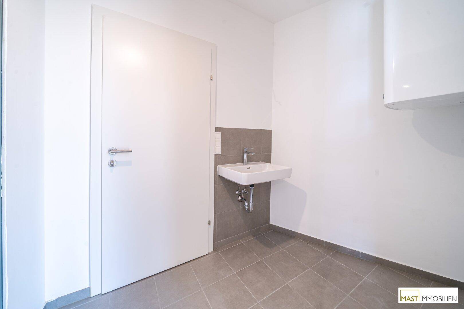 Modernes WC mit Fliesenboden, Waschbecken und einem Warmwasserbereiter an der Wand.
