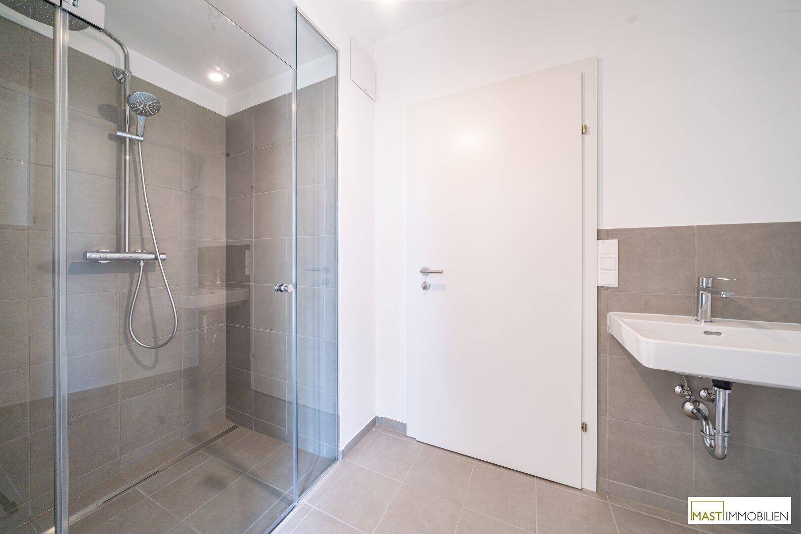 Modernes Badezimmer mit begehbarer Dusche, Waschbecken und grauen Fliesen an Boden und Wänden.