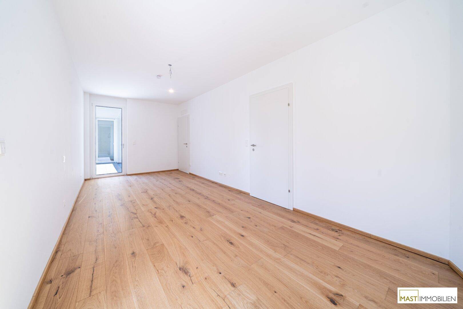 Helles Schlafzimmer mit Holzboden und weißer Tür, das einen Zugang zu einem weiteren Bereich bietet.