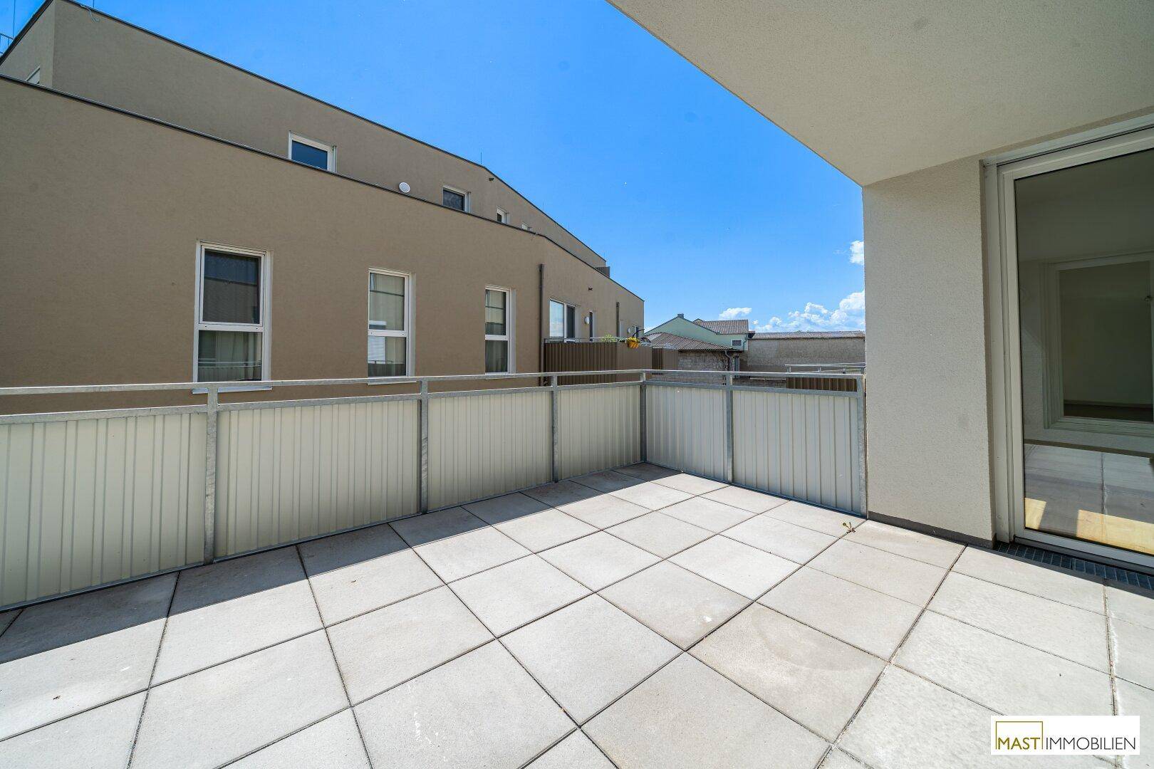 Große, geflieste Terrasse mit Blick auf die umliegenden Gebäude und den blauen Himmel.