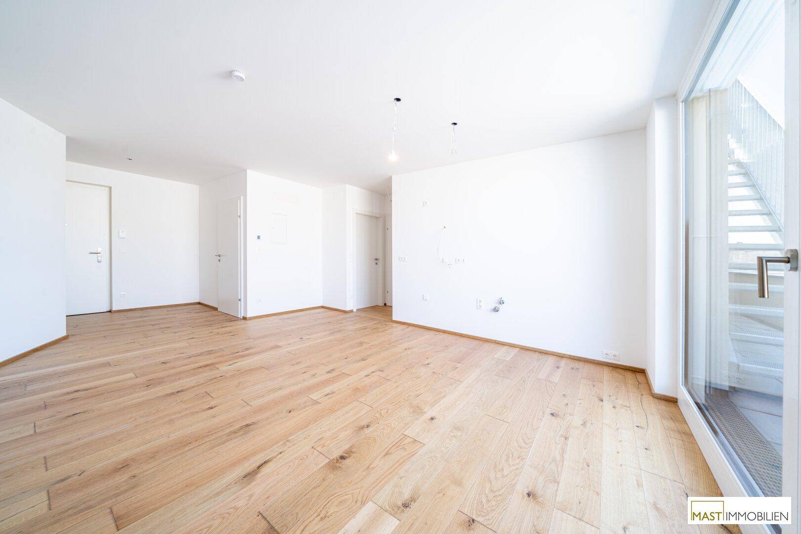 Lichtdurchfluteter Wohnraum mit Zugang zu einem Balkon und hellem Holzfußboden.