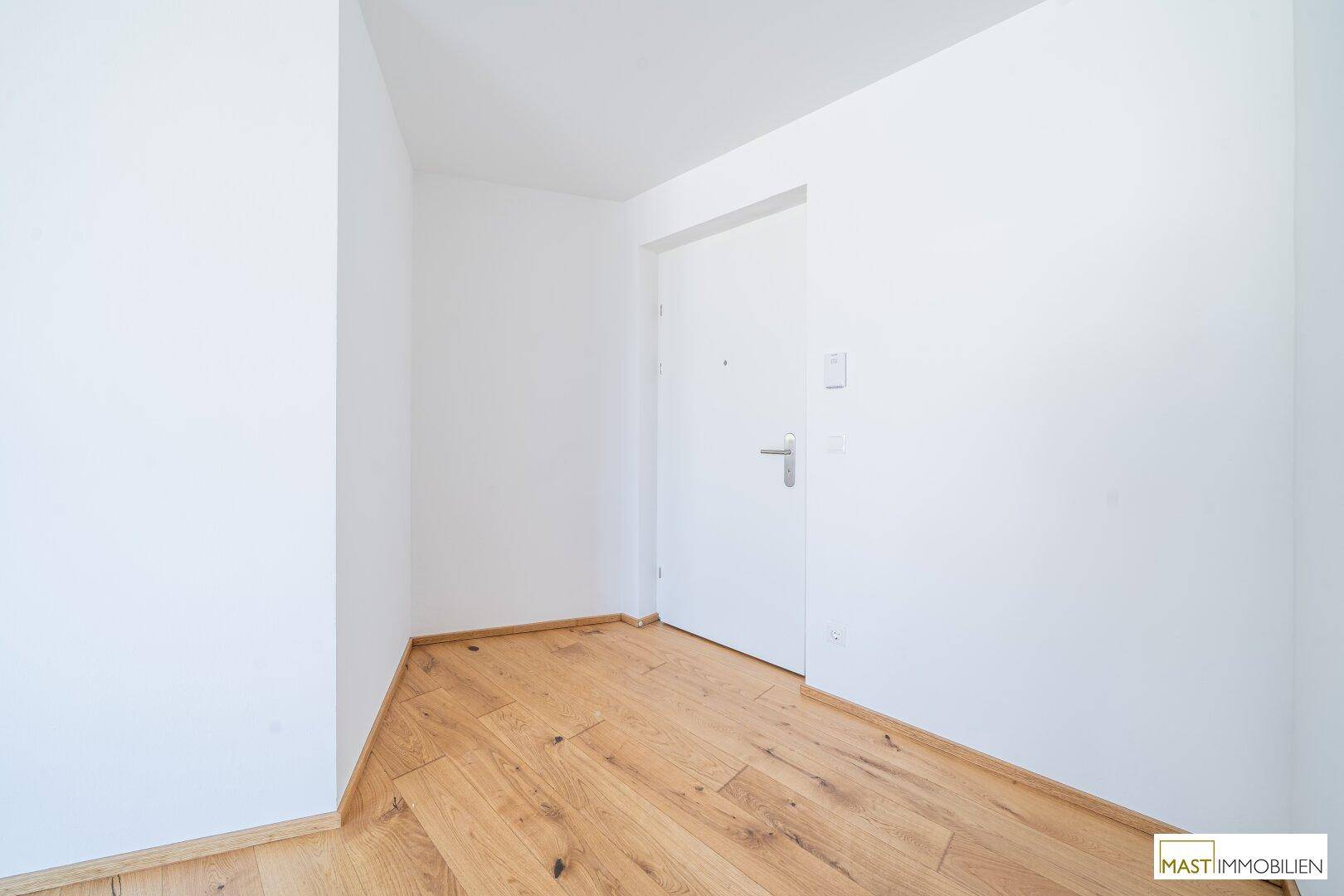 Heller Eingangsbereich mit Holzparkettboden und weißer Eingangstür.