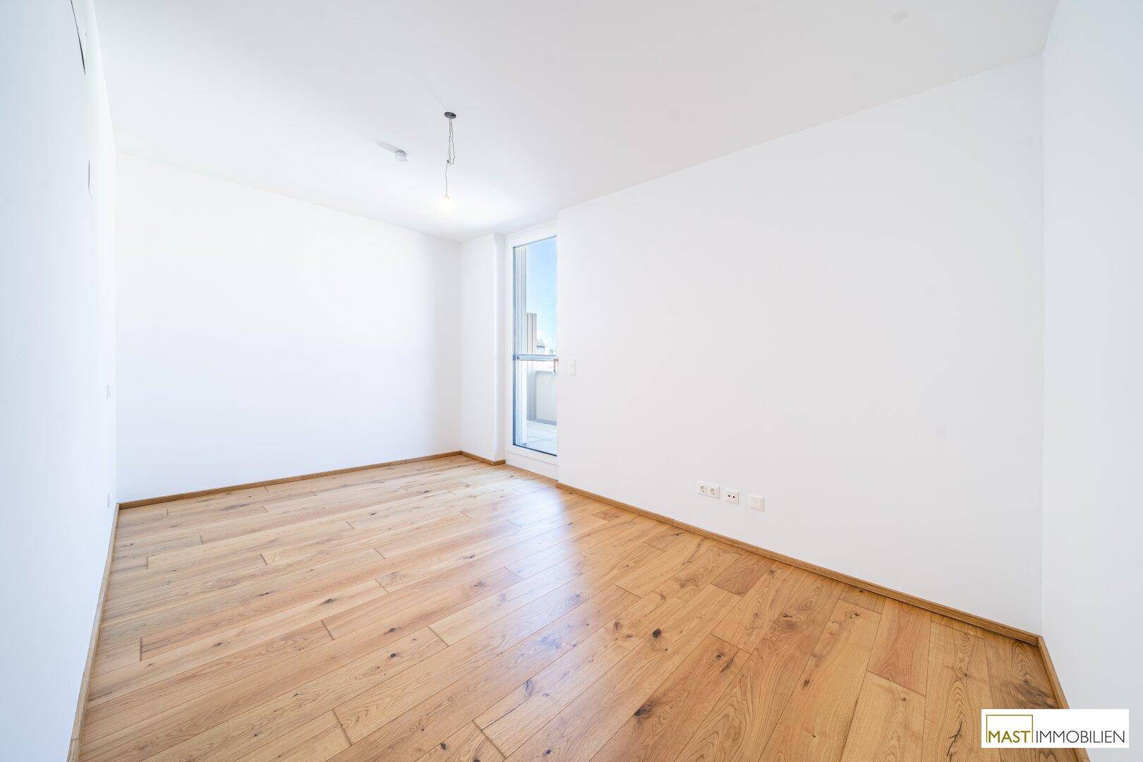Helles Schlafzimmer mit Holzparkettboden und Zugang zu einem kleinen Balkon.