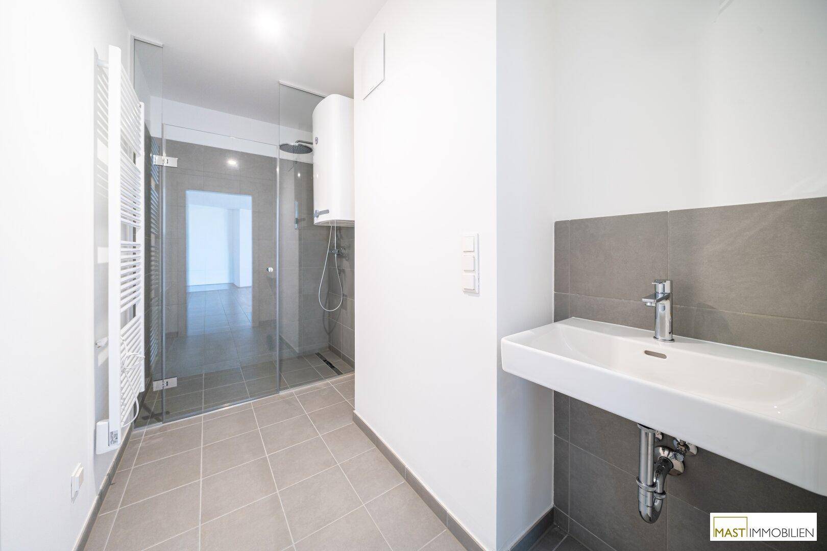 Modernes Badezimmer mit ebenerdiger Dusche, Handtuchheizkörper und Waschbecken.