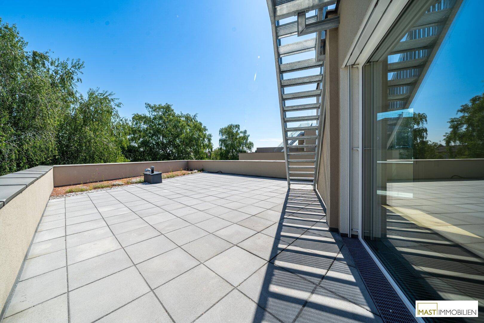 Geräumige Dachterrasse mit modernen Pflastersteinen und einer Außentreppe, umgeben von Grün.