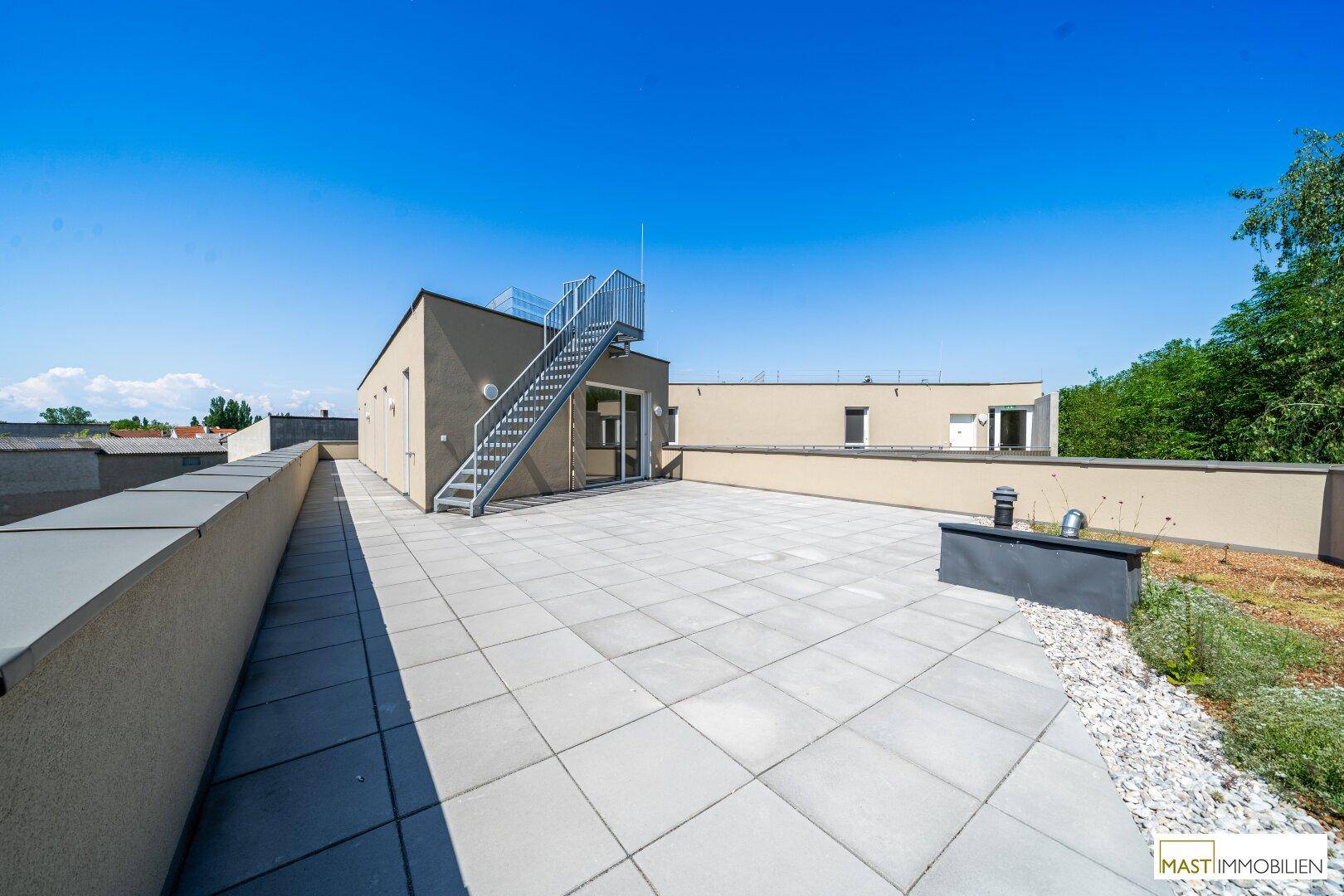 Weitläufige Dachterrasse mit Blick auf die Umgebung und Zugang über eine moderne Außentreppe.