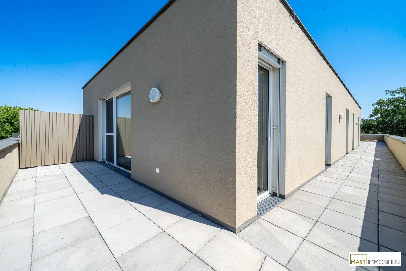Eckbereich der Dachterrasse mit hellen Pflastersteinen und moderner Fassade des Gebäudes.