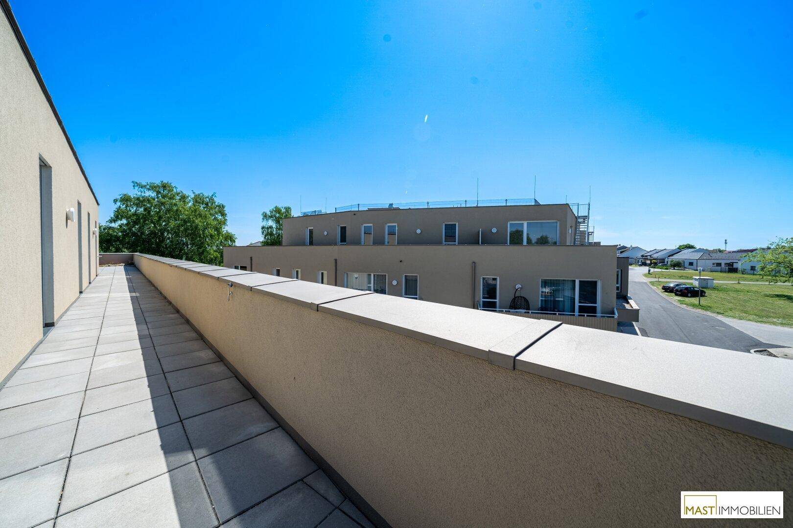 Blick von der Dachterrasse entlang der Gebäudefassade auf die umliegende Bebauung und Straße.