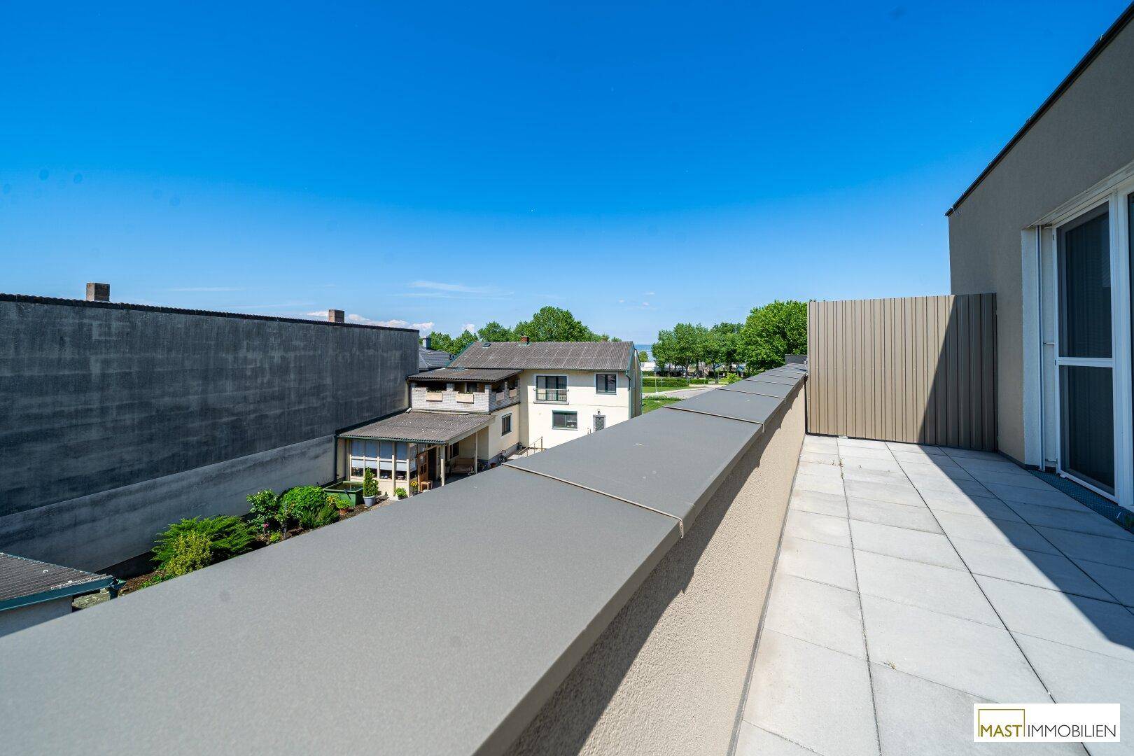 Aussicht von der Dachterrasse über eine Mauer auf ein benachbartes Haus und grüne Bäume.