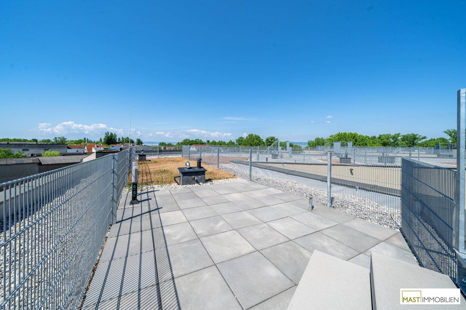Teil der Dachterrasse mit grauen Pflastersteinen und Metallzäunen, umgeben von Kiesflächen.