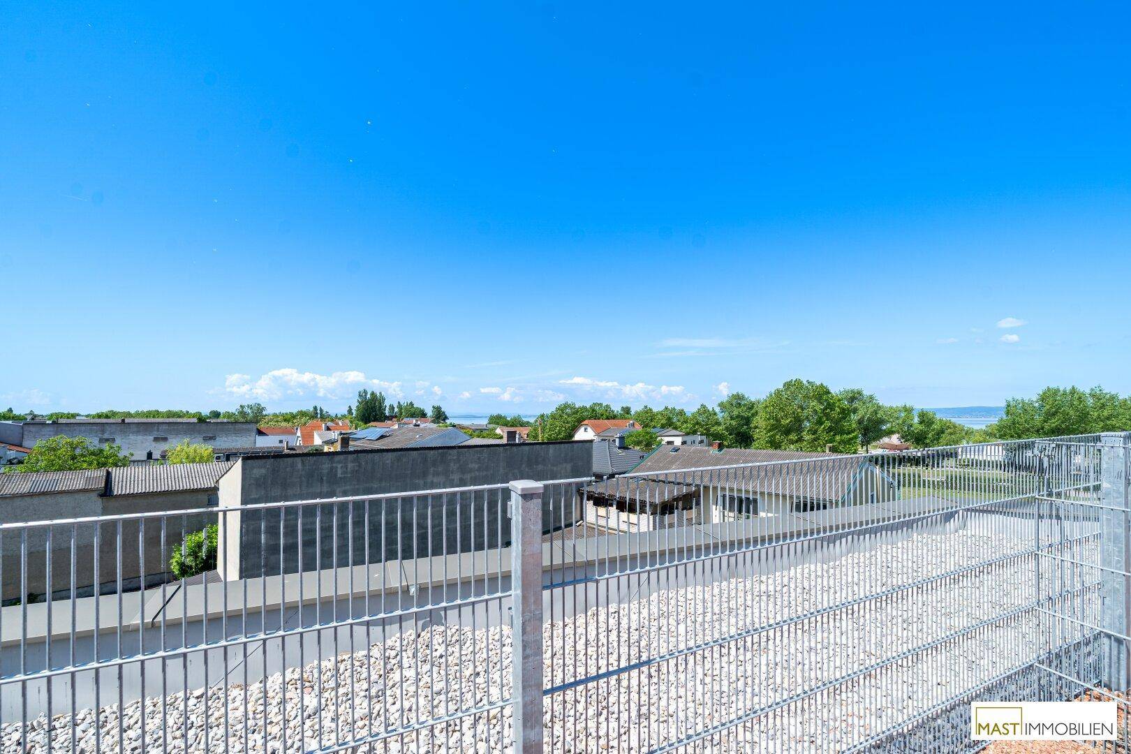 Weitblick von der Dachterrasse über die Umgebung mit Gebäuden und einem See am Horizont.