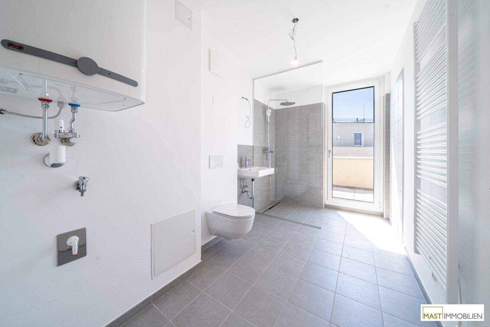 Modernes Badezimmer mit grauen Fliesen, begehbarer Dusche und wandhängendem WC, hell und funktional.