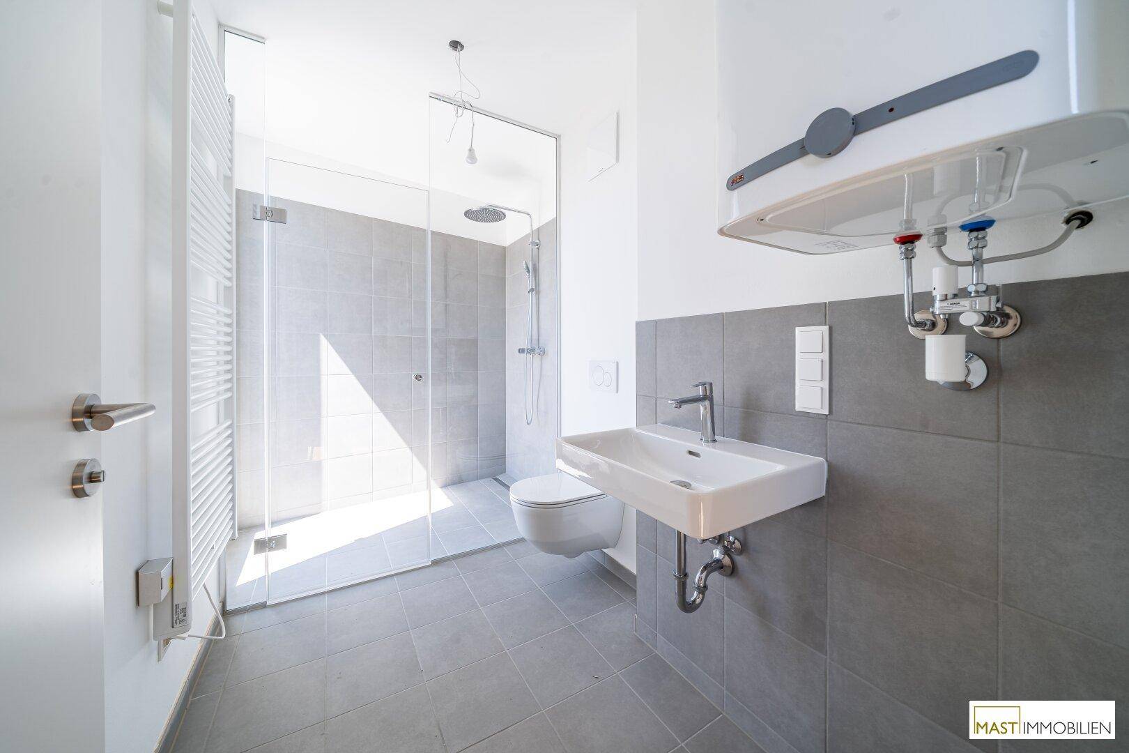 Helles, modernes Badezimmer mit großzügiger begehbarer Dusche, elegantem Waschbecken und grauen Fliesen.