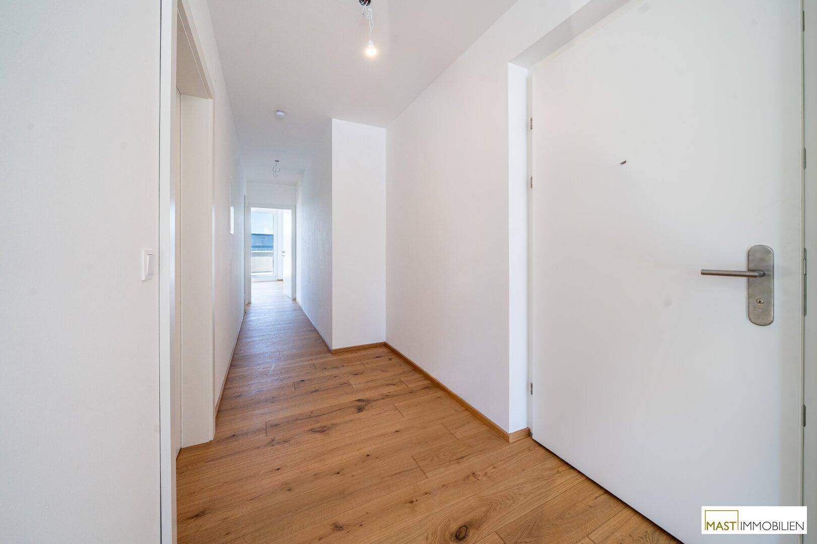 Langer, heller Flur mit Holzboden und weißen Wänden, der verschiedene Räume miteinander verbindet.