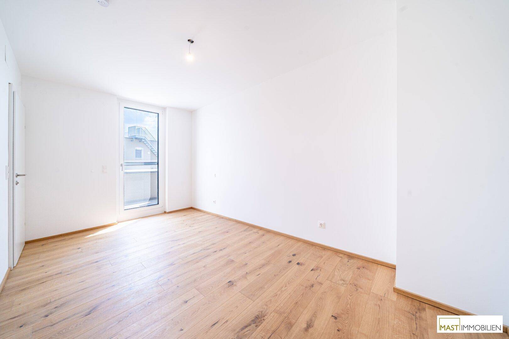 Lichtdurchflutetes Zimmer mit Holzboden und weiß gestrichenen Wänden, ideal als Schlafzimmer.