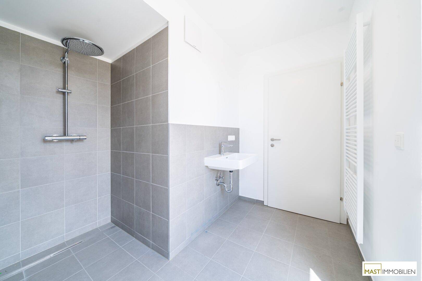 Modernes Badezimmer mit grauen Fliesen, ebenerdiger Dusche und Regenbrause.