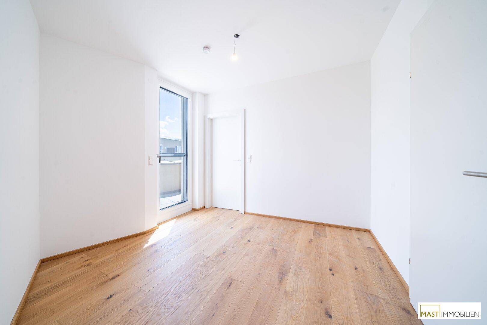 Helles Schlafzimmer mit Holzboden und Zugang zu einem kleinen Balkon.