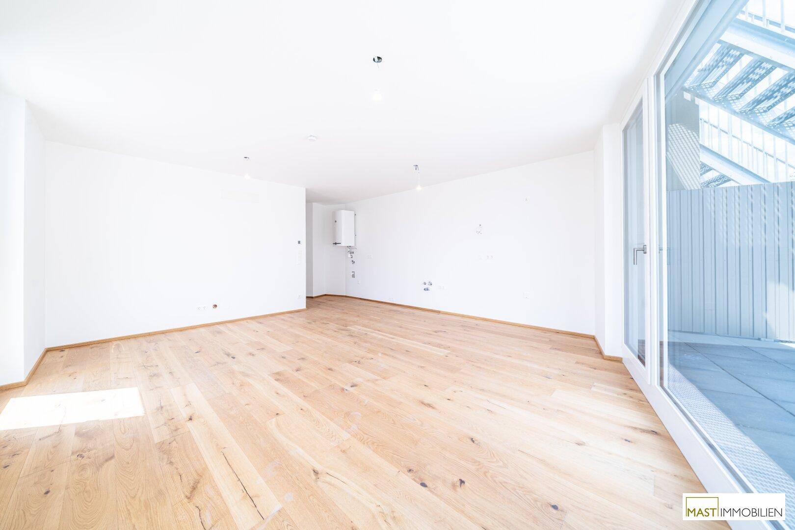 Geräumiger, heller Innenraum mit Holzboden und Zugang zu einem Außenbereich.