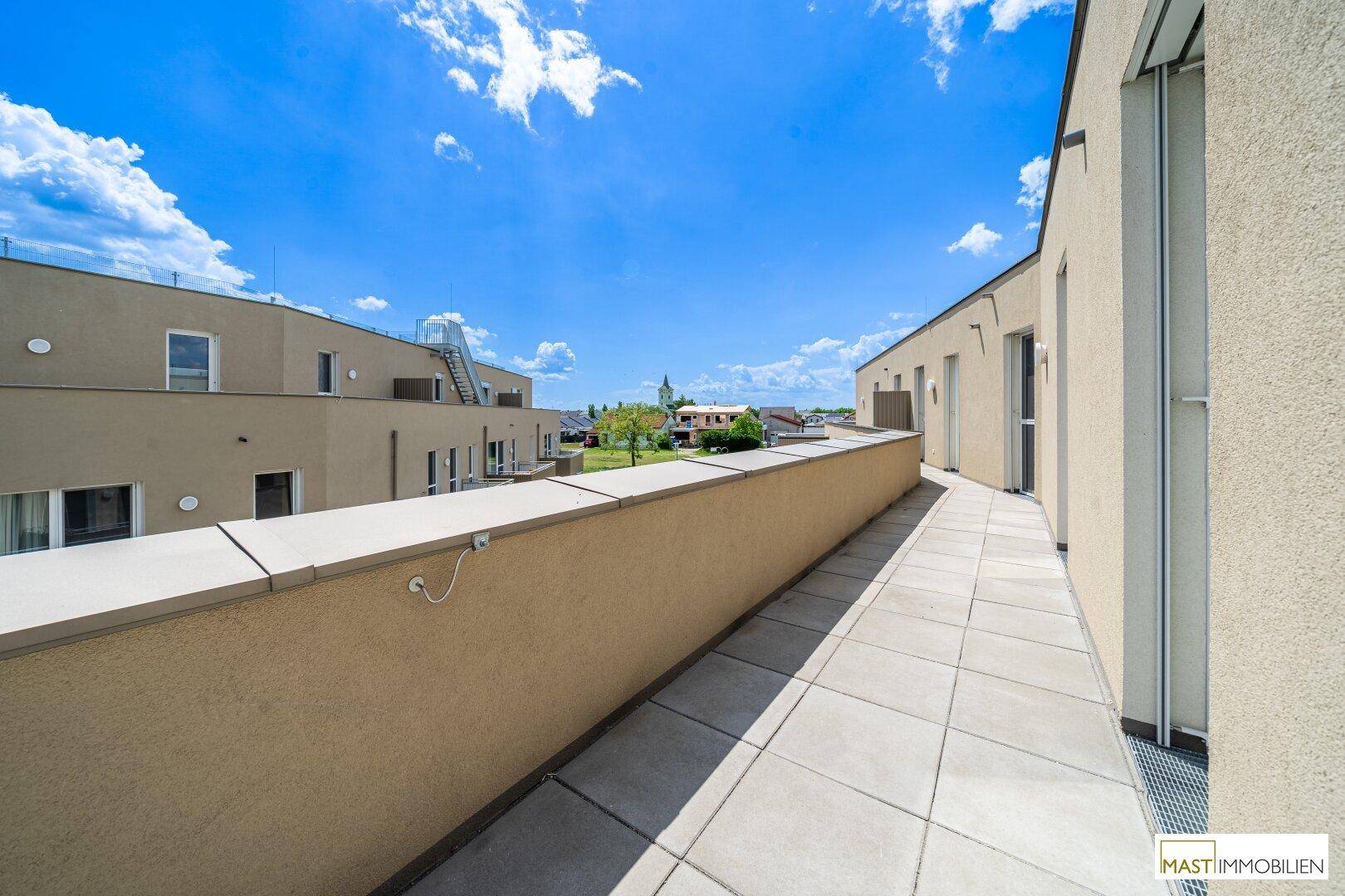 Langer Balkon entlang der Gebäudefassade mit Blick auf die Umgebung.