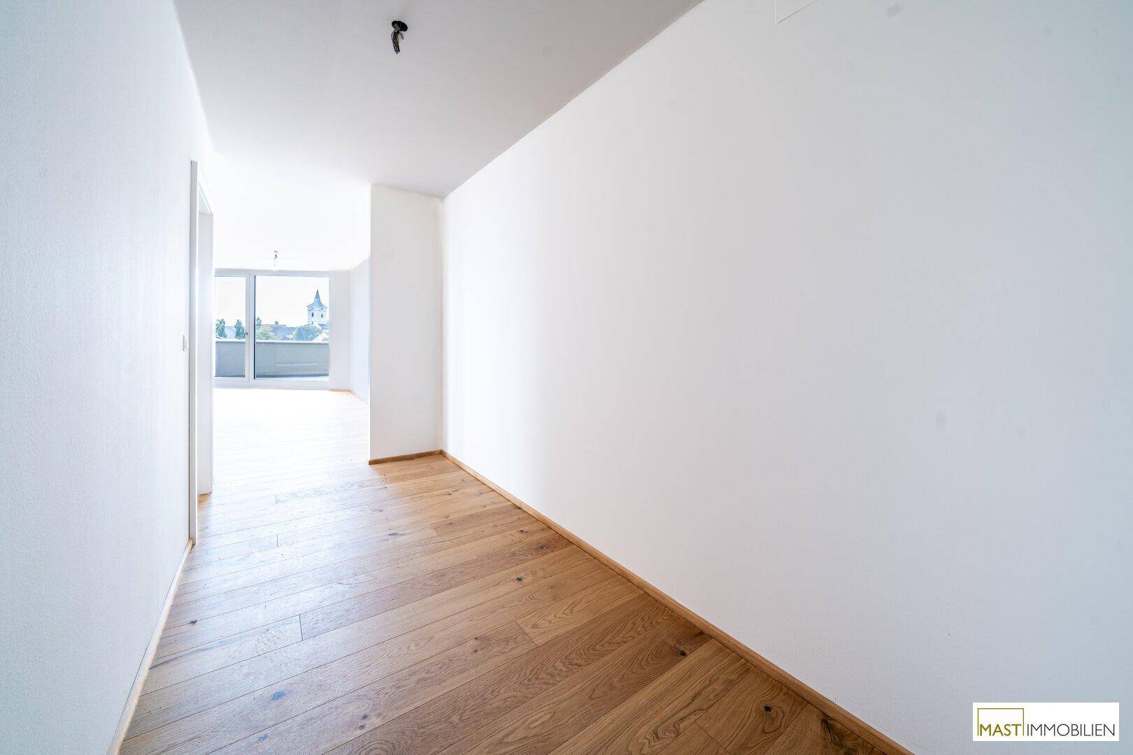 Langer, heller Flur mit Holzboden, der in einen lichtdurchfluteten Wohnbereich mündet.
