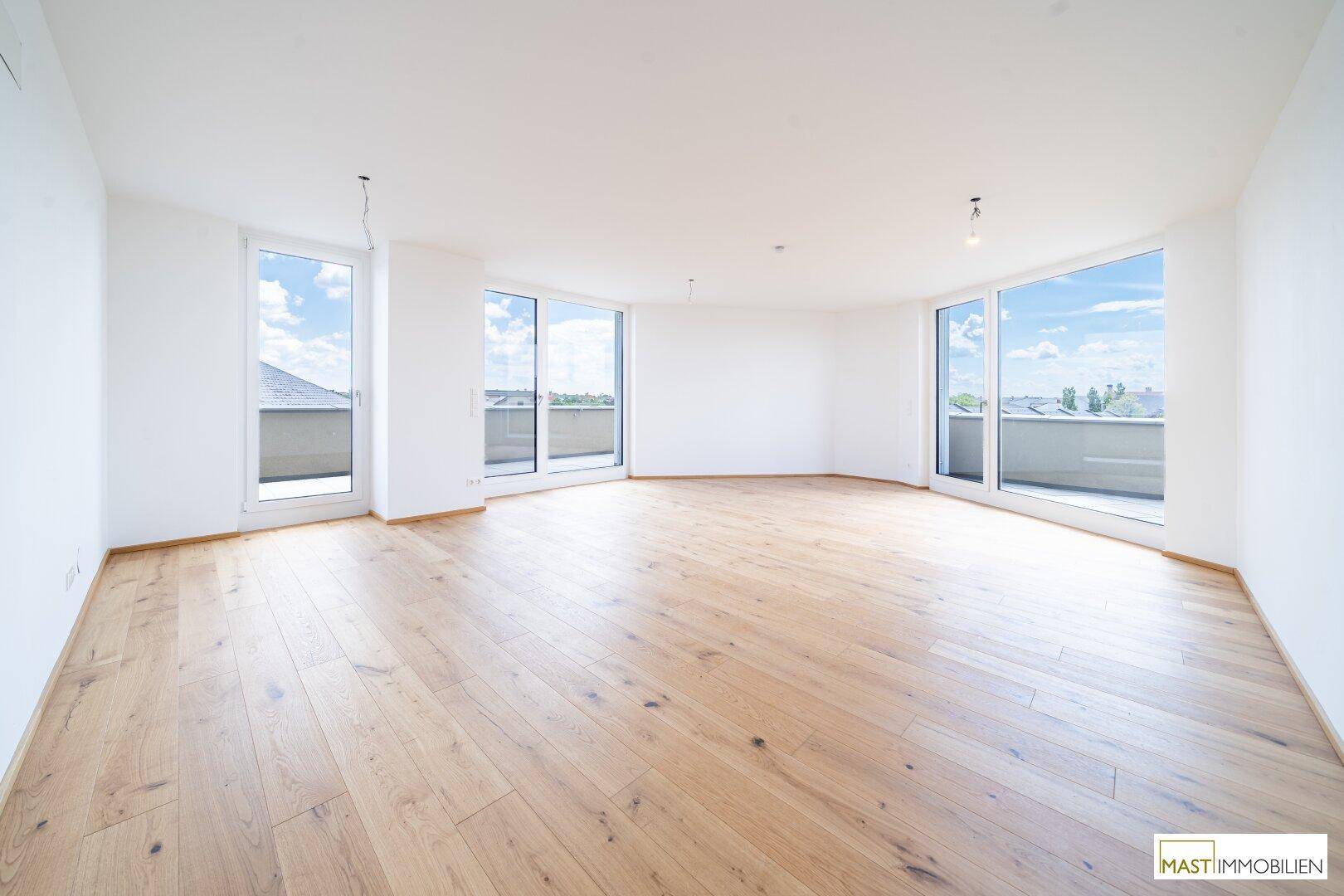 Geräumiges, lichtdurchflutetes Wohnzimmer mit Holzboden und mehreren Zugängen zum Außenbereich.
