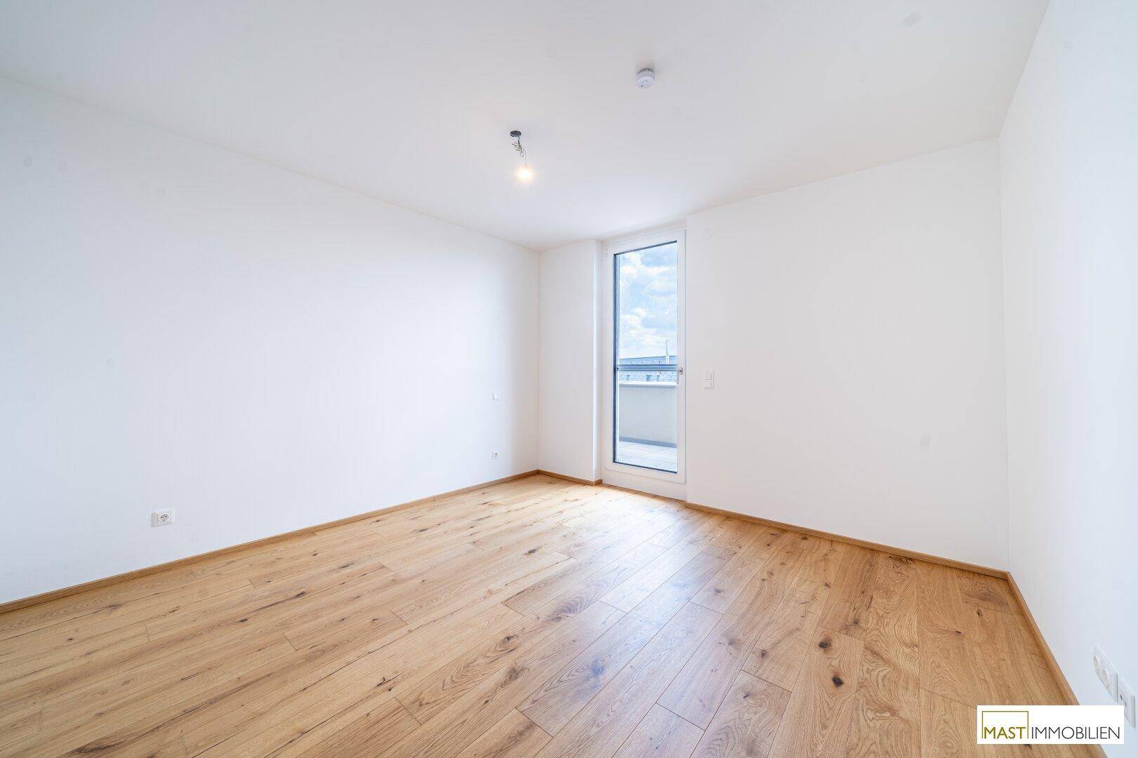 Helles Schlafzimmer mit Holzboden und Fenster, das den Raum mit Tageslicht erfüllt.