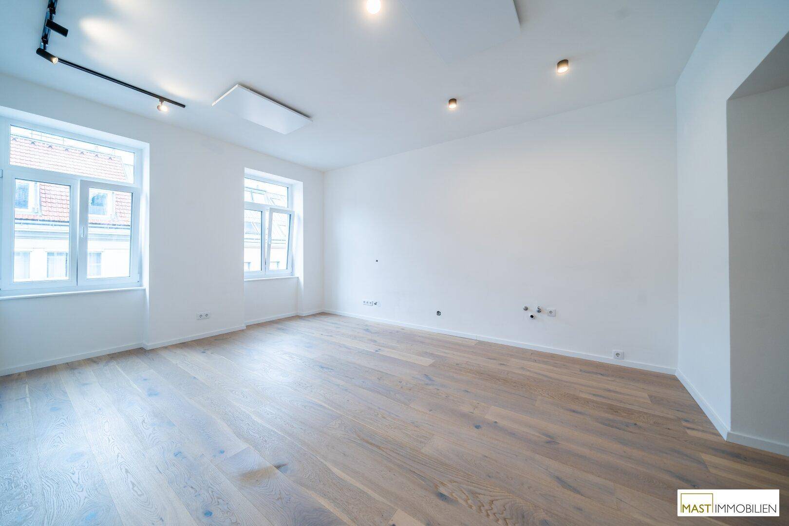 Geräumiger, heller Raum mit Holzboden, weißen Wänden und moderner Deckenbeleuchtung.