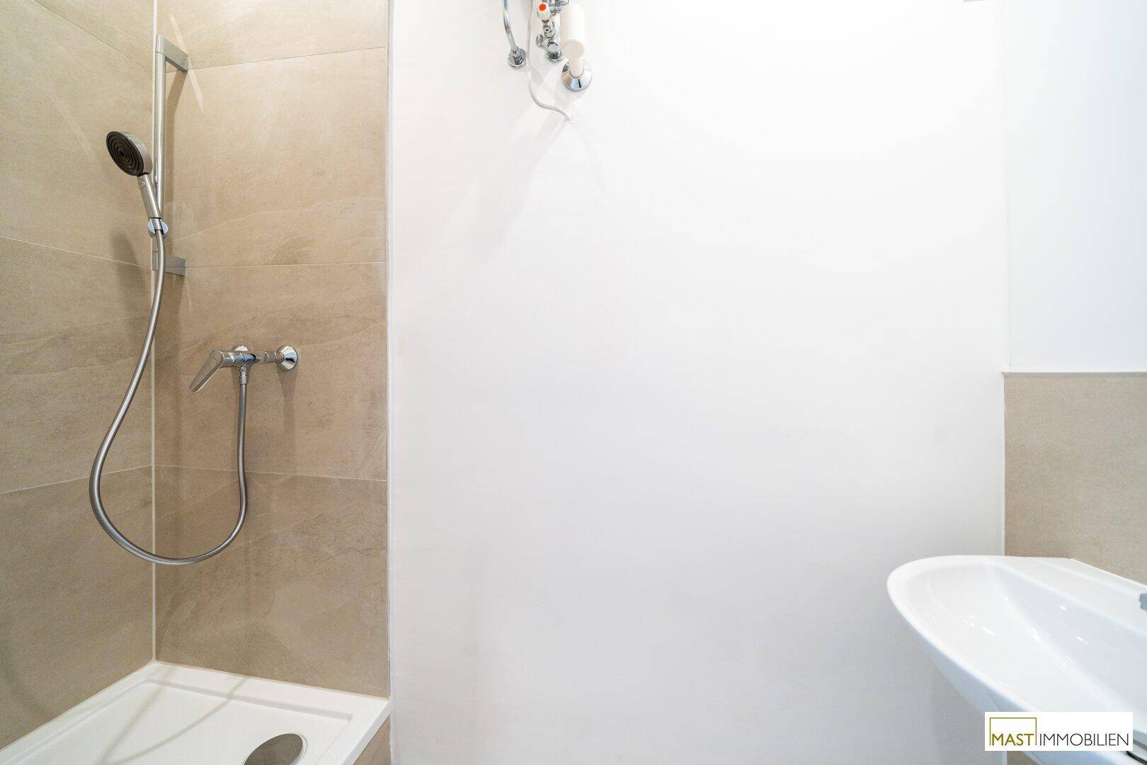 Badezimmer mit Duschbereich, modernem Waschbecken und hellen Fliesen an den Wänden.