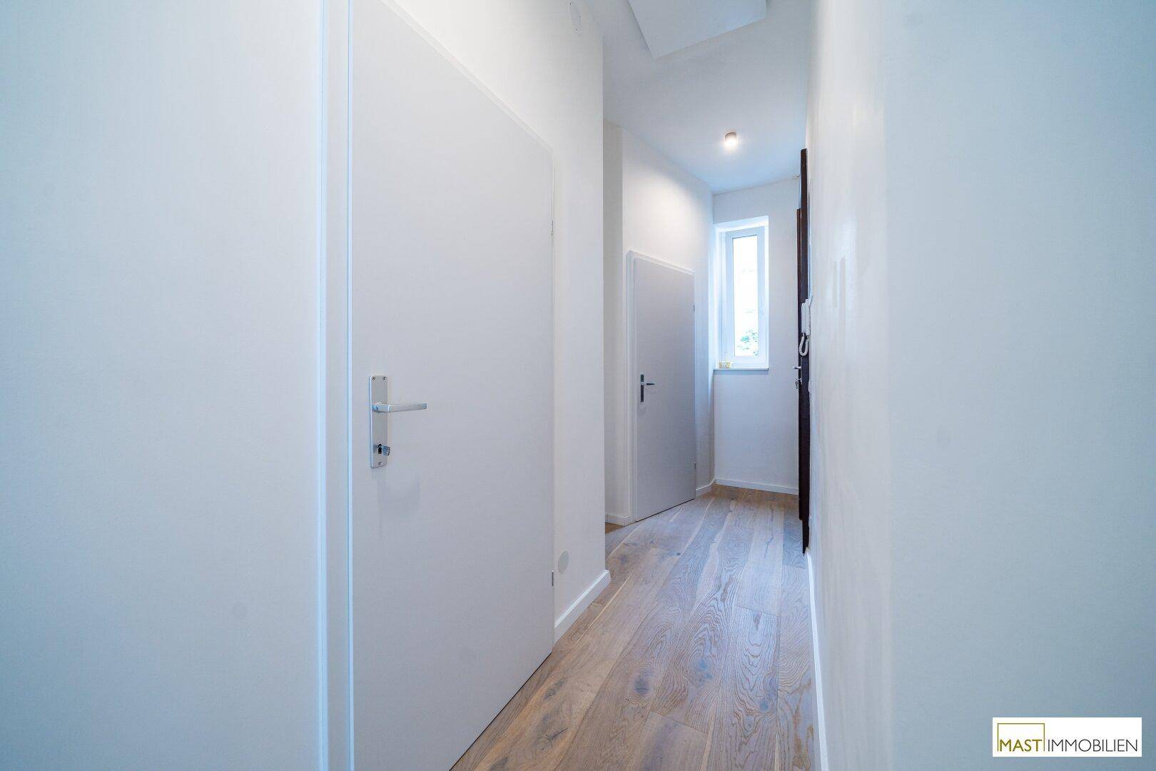 Heller Flur mit Holzboden und weißen Türen, der zu weiteren Räumen führt.