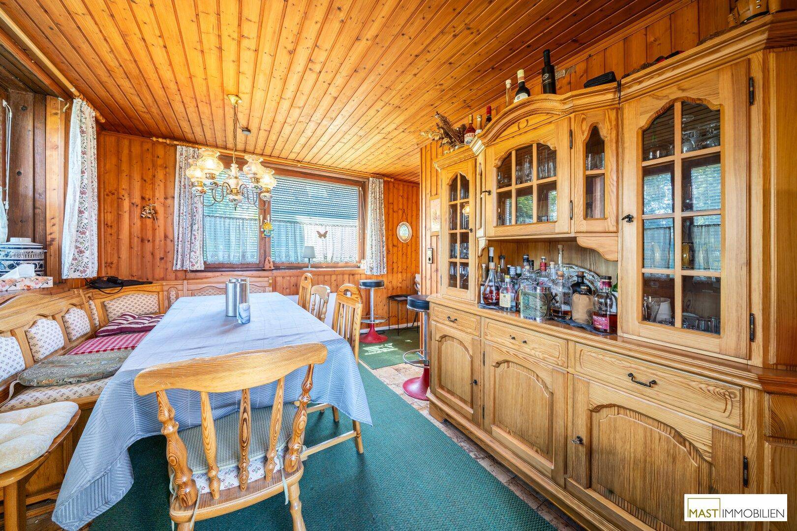 Traditioneller Essbereich mit großem Holzschrank, Esstisch und Holzvertäfelung an Wänden und Decke.