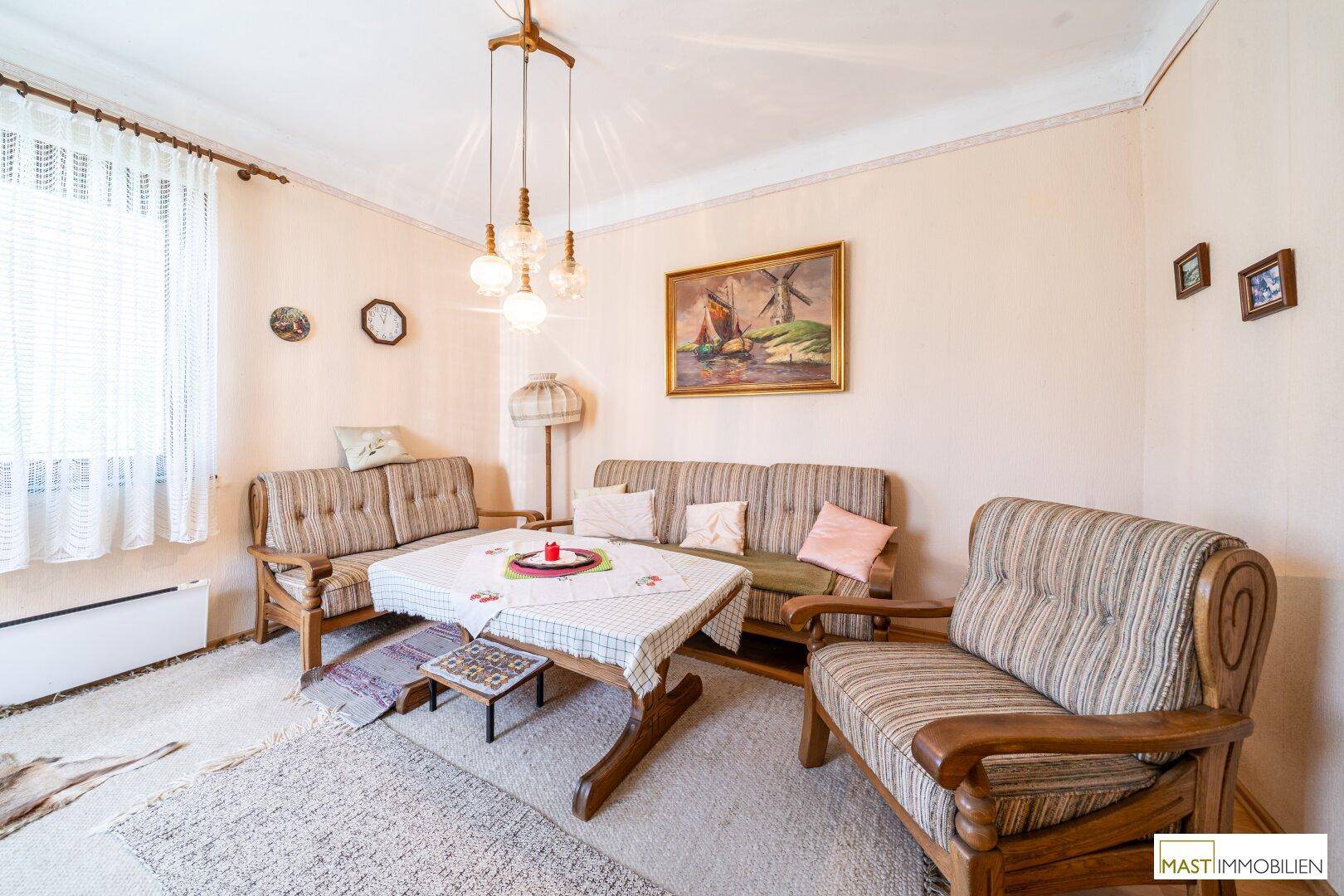 Helles Wohnzimmer mit traditionellen Möbeln, Teppichboden und einem Fenster mit Vorhängen.