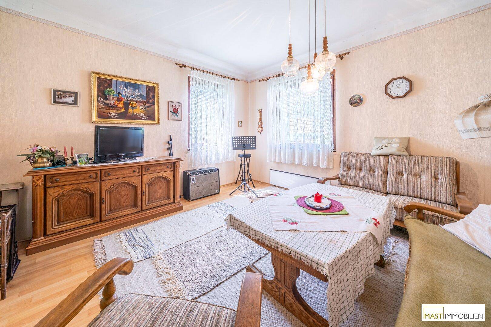 Wohnzimmer mit traditionellen Holzmöbeln, Teppich und einem Fernseher auf einem Sideboard.