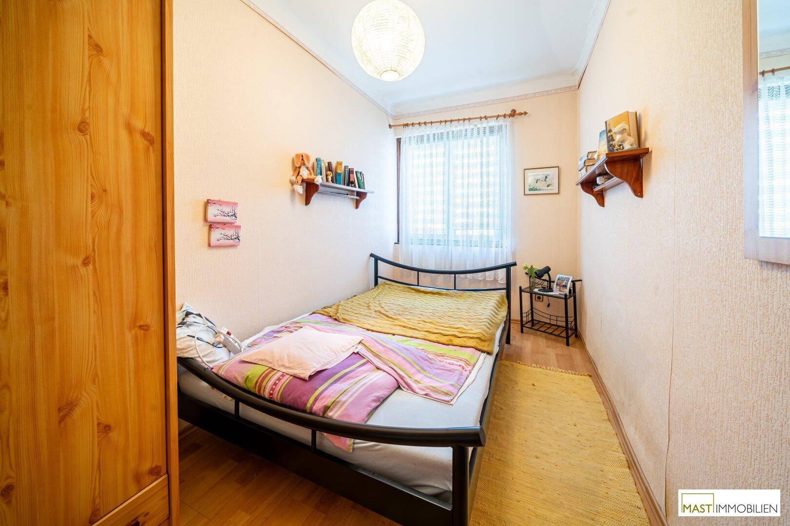 Kleines Schlafzimmer mit Einzelbett, Holzschrank und einem Fenster mit Vorhängen.