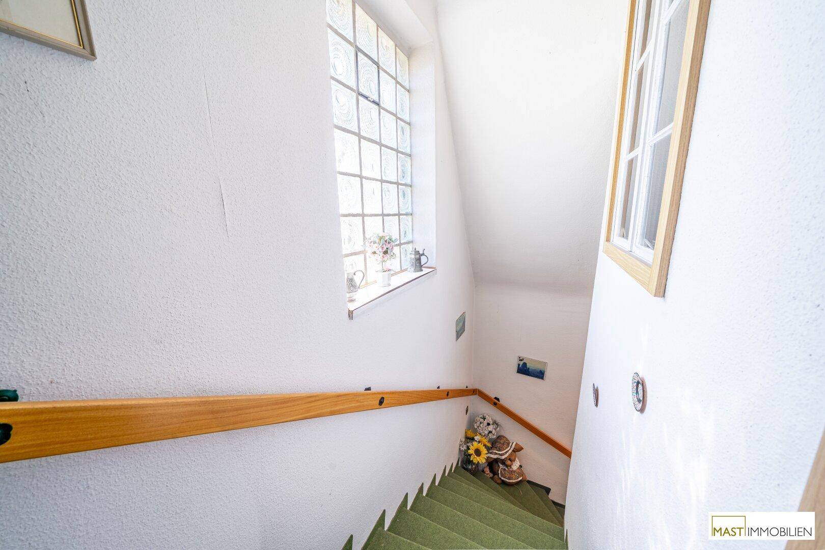 Treppenhaus mit grünem Teppichboden und einem Fenster, das Tageslicht hereinlässt.