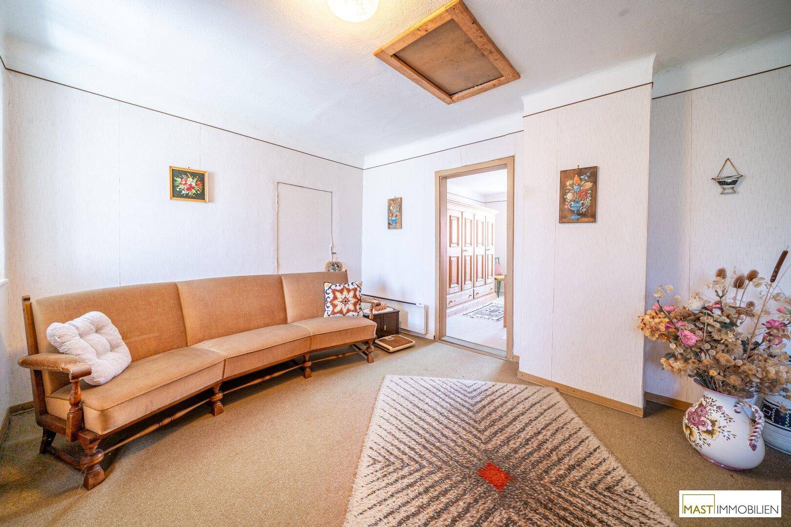 Geräumiges Wohnzimmer mit langer Couch, Teppichboden und schlichten weißen Wänden.