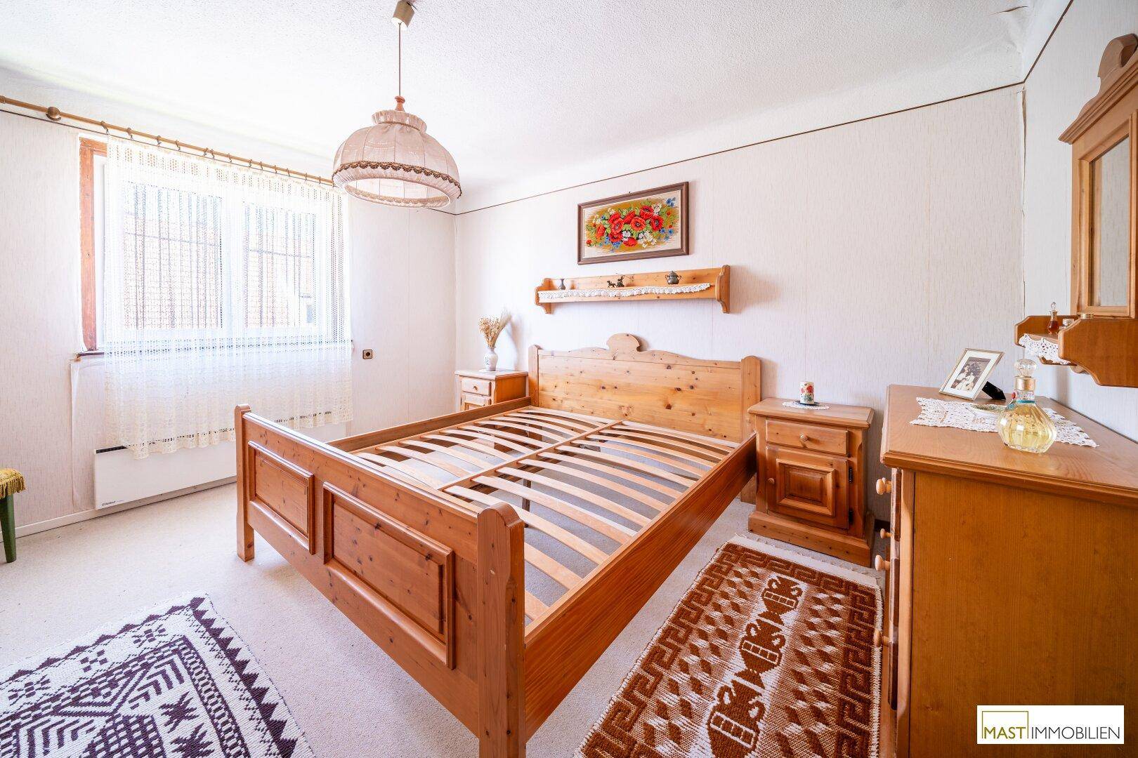 Helles Schlafzimmer mit Doppelbett aus hellem Holz und einem Fenster mit Blick nach draußen.