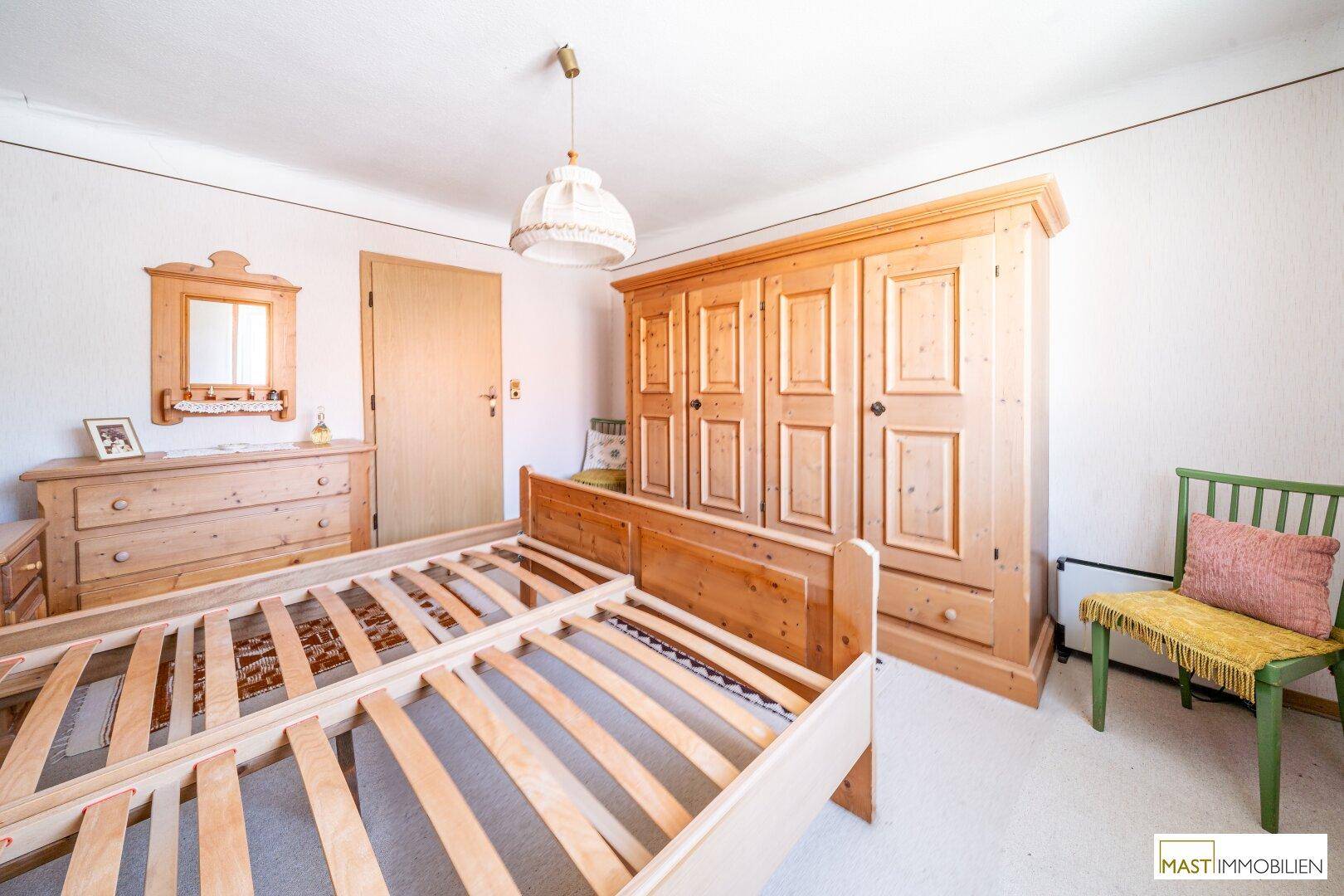 Schlafzimmer mit großem Holzschrank, Doppelbett und einem Fenster, das viel Licht spendet.