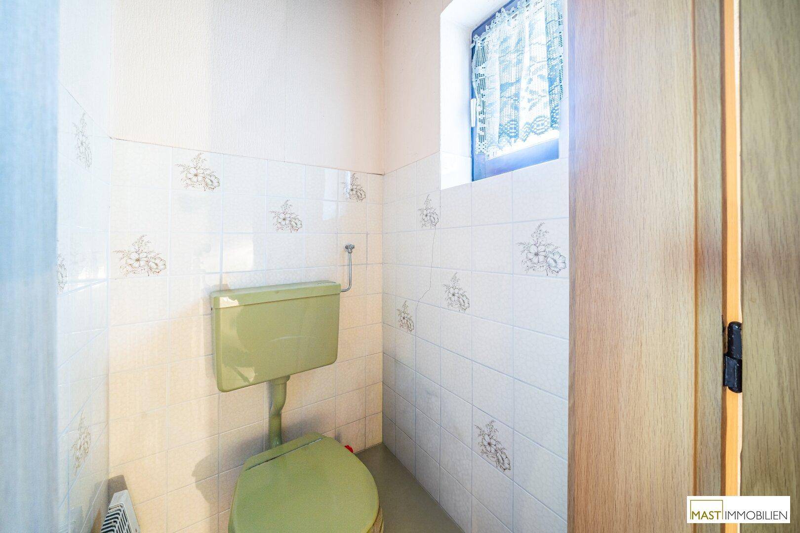 Separate Toilette mit hellgrüner Keramik und weißen Fliesen an den Wänden.