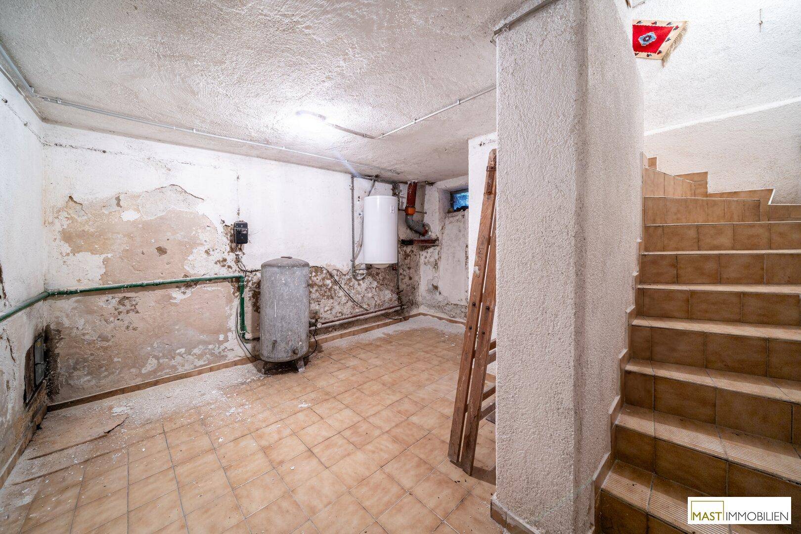 Unfertiger Kellerraum mit sichtbaren Rohren, Boiler und einer Treppe.
