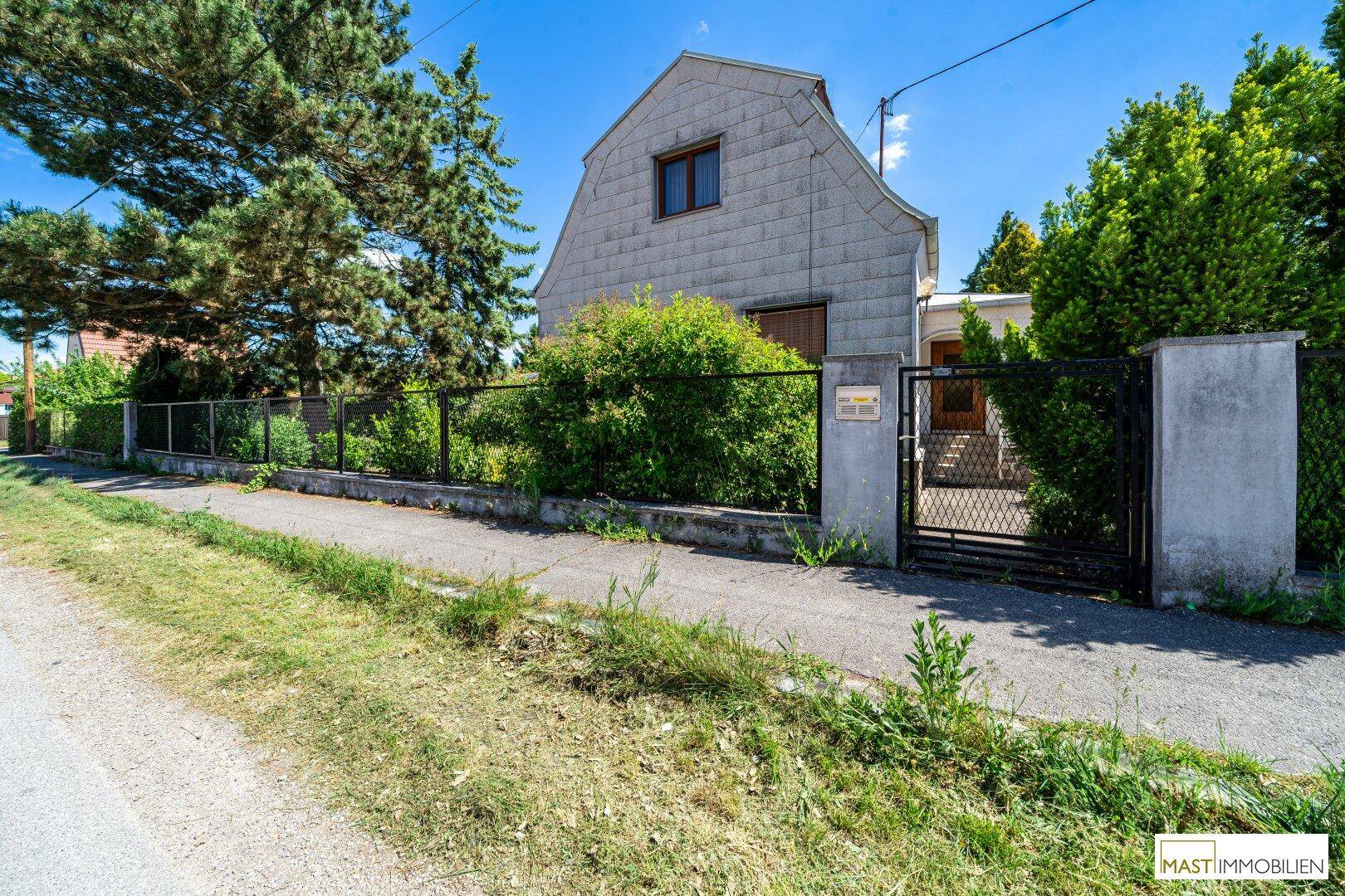 Ansicht des Einfamilienhauses von der Straße mit Zaun und Hecke.